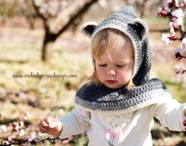 A child in a garden with a hooded crochet cowl.