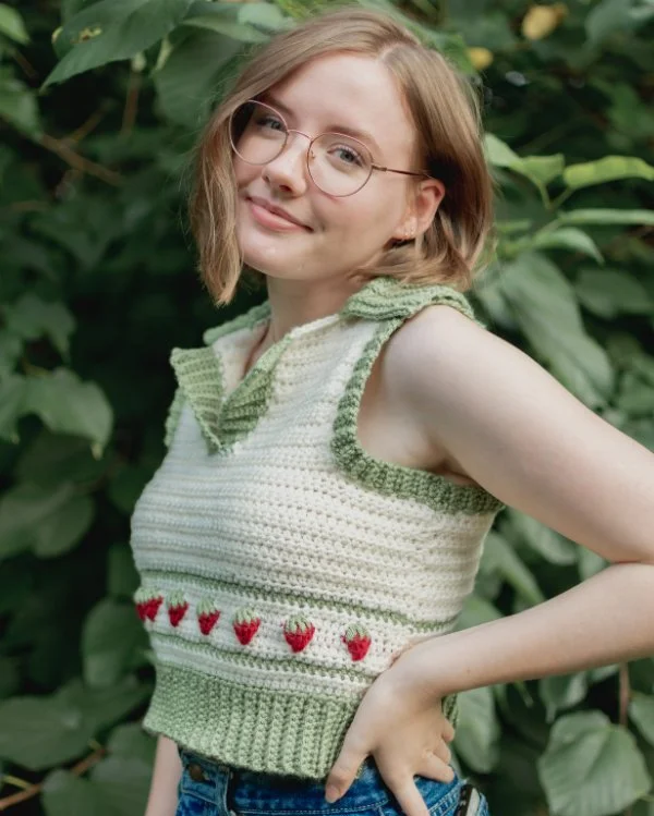 A woman wearing a cropped crochet sweater vest with v-neck, collar, and strawberry motifs.