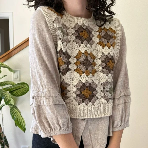 A woman wearing a granny square sweater vest in browns and neutrals.