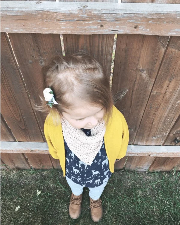 A child in a yellow jacket wearing a crochet cowl.