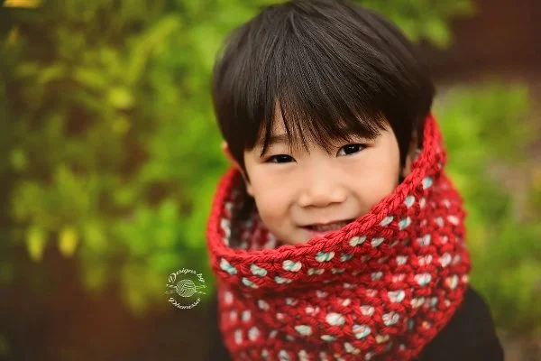A boy in a garden wearing a brightly coloured tunisian crochet cowl.