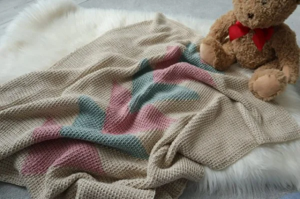 A Tunisian crochet baby blanket next to a teddy bear.
