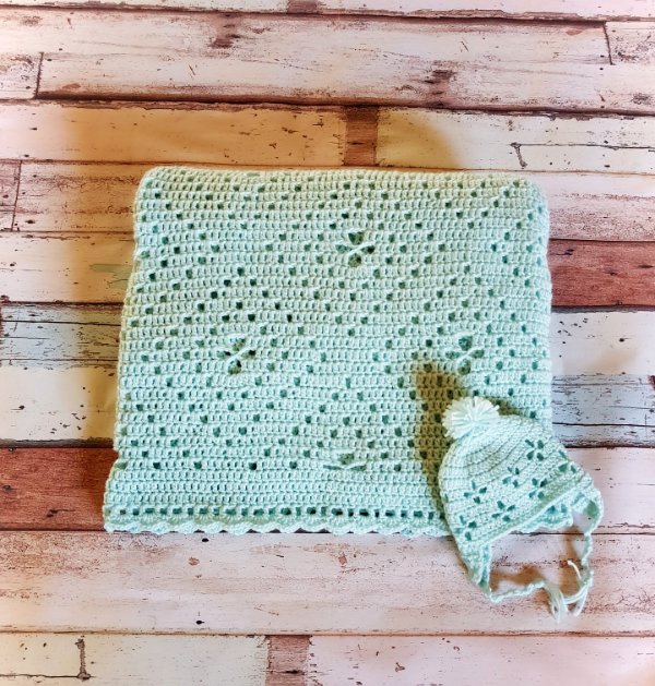 A folded filet crochet baby blanket and a matching baby hat.
