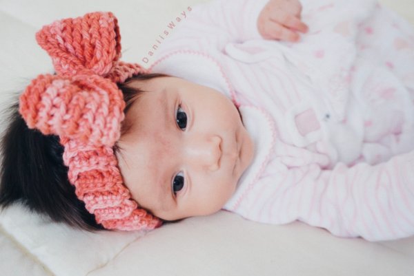 A newborn baby wearing a bright pink crochet headband.