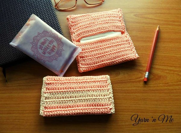 Two crochet tissue holders on a desk with glasses and a pencil.
