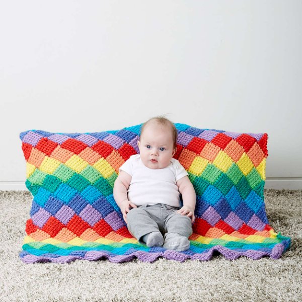 A baby sitting on a bright rainbow-coloured Tunisian crochet baby blanket.