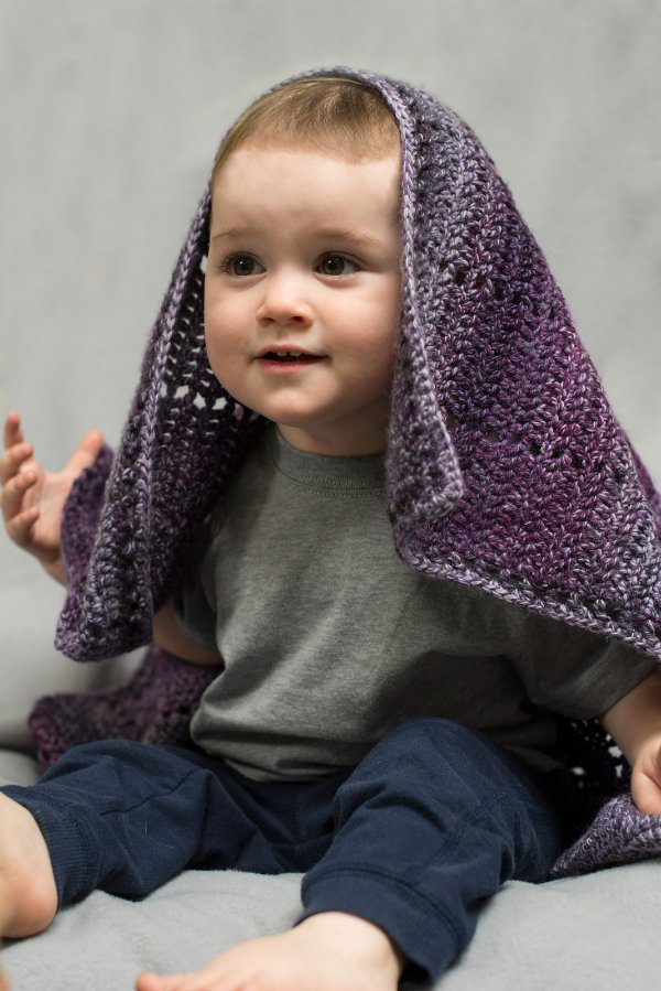 A baby with a filet crochet blanket draped over him.