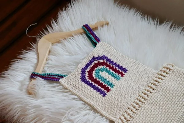 A rainbow detail crochet baby romper laid on a fur rug.