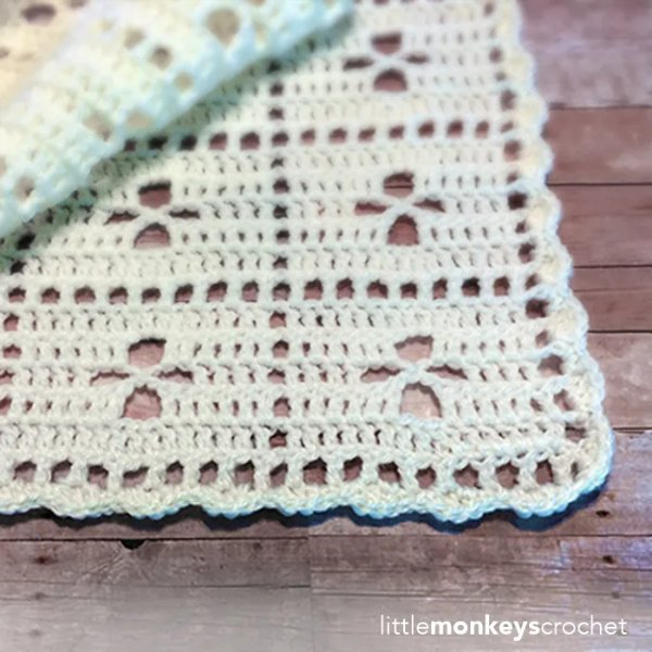 A filet crochet baby blanket on a timber board background.