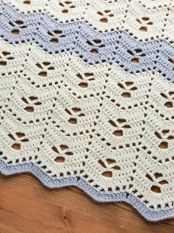 A lavender blue and white rippled filet crochet baby blanket.