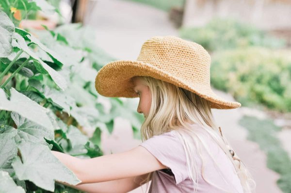 A young girl in a garden wearing a fedora-style crochet sun hat.