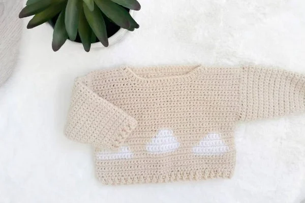 A crochet baby sweater with colourwork cloud motifs.
