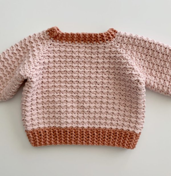 A two-tone pink crochet baby sweater.