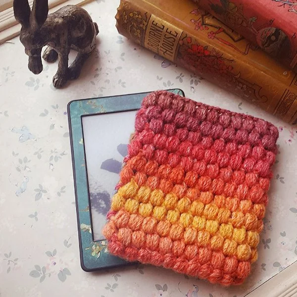 A puff-stitch crochet Kindle cover in gradient yarn.