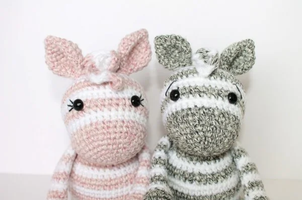 Two crochet zebra toys - one pink and white, one grey and white.