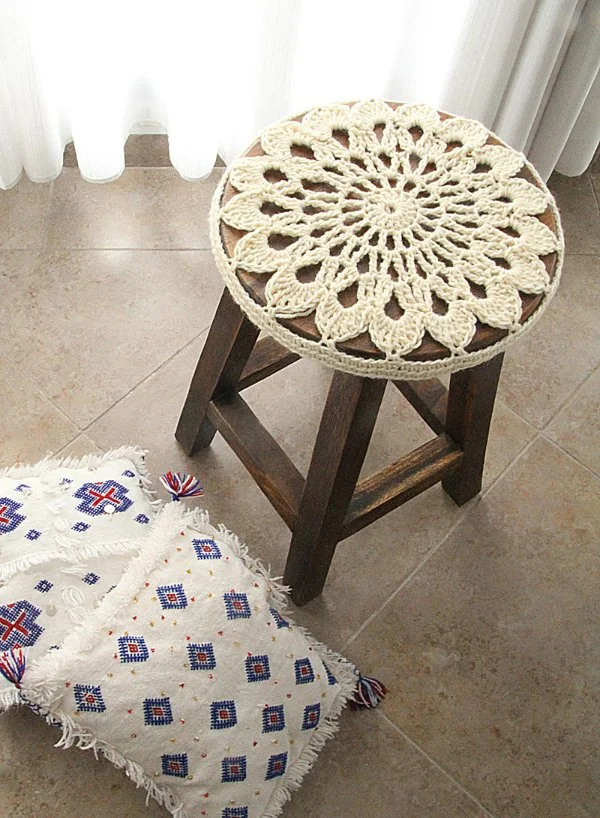 Cream coloured crochet stool cover on a dark timber stool and cushions.