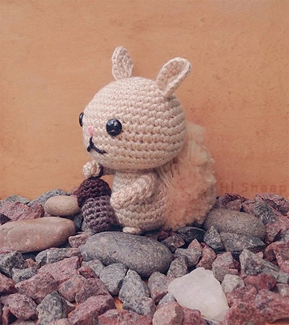 A little crochet squirrel on a bed of rocks holding an acorn.