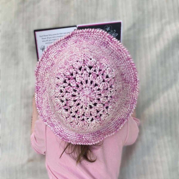 Top view of a child reading a book while wearing a pink crochet sun hat.