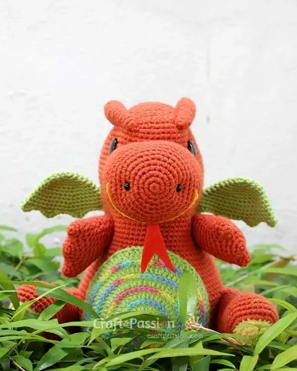 A colourful crochet dragon sitting on a pile of leaves.