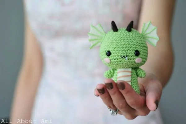 A cute little crochet dragon sitting in the palm of a hand.