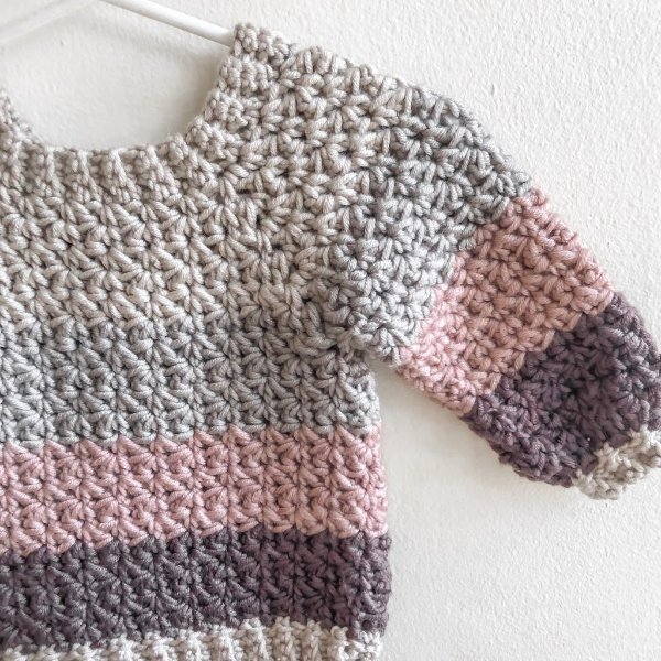 A striped crochet baby sweater made in chunky yarn.