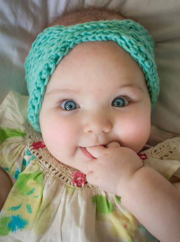 A young baby wearing a bright turquoise crochet headband.