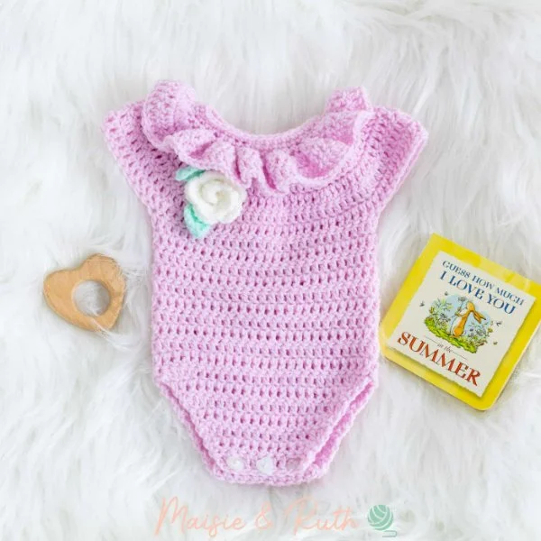 A frilly pink crochet baby romper on a white fur rug with baby toys.