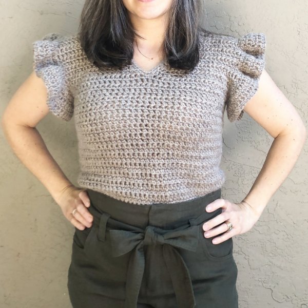 A woman in a grey-brown crochet tee with frilled sleeves.