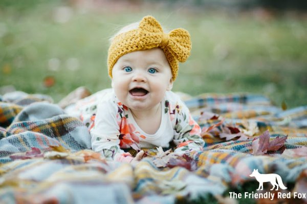 A baby in a picnic rug wearing a yellow crochet headband.