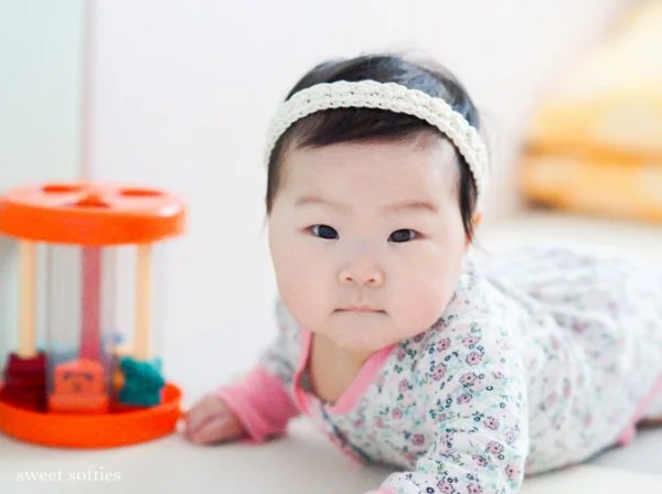 A young baby wearing a simple white lace crochet headband.