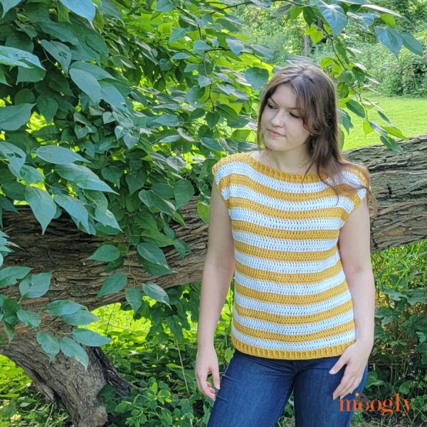 A woman outdoors wearing a yellow and white striped crochet tee.