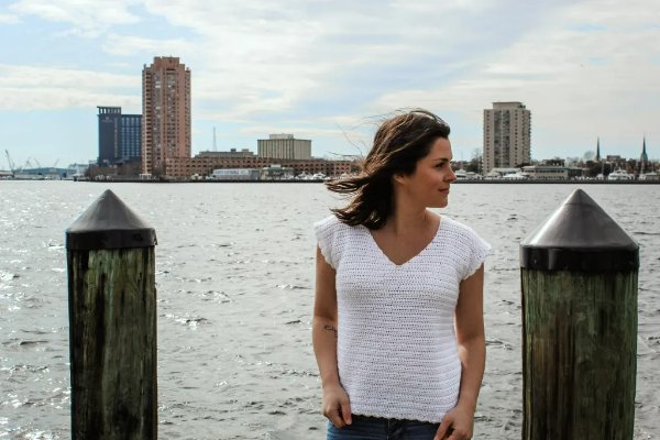 A woman on a dock wearing a white v-neck crochet tee.