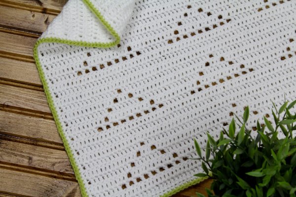 A white filet crochet blanket with triangle motifs.