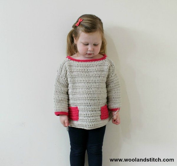 A young child wearing a crochet seater with contrasting coloured pockets.