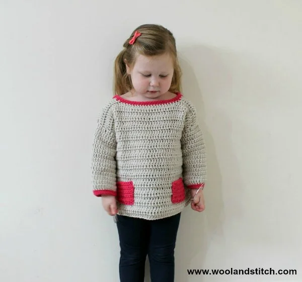 A young child wearing a crochet seater with contrasting coloured pockets.