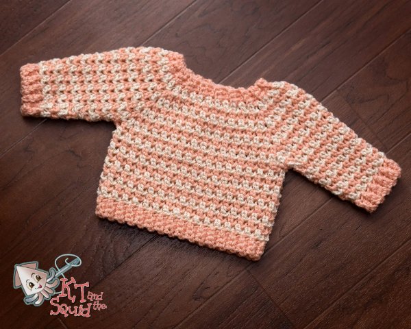 A striped crochet baby sweater on a timber background.