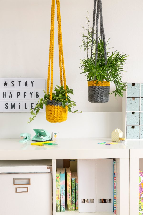 A home office with two plants hanging in yellow and grey crochet plant hangers.