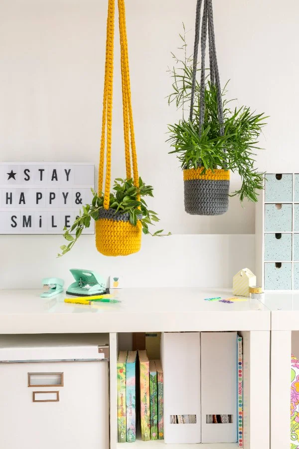 A home office with two plants hanging in yellow and grey crochet plant hangers.