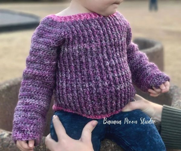 A toddler wearing a crochet sweater.