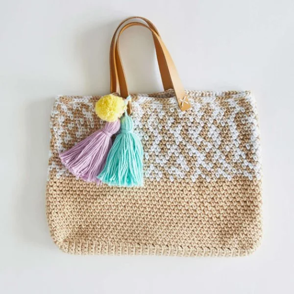 A crochet beach tote with coloured pompom and tassels.