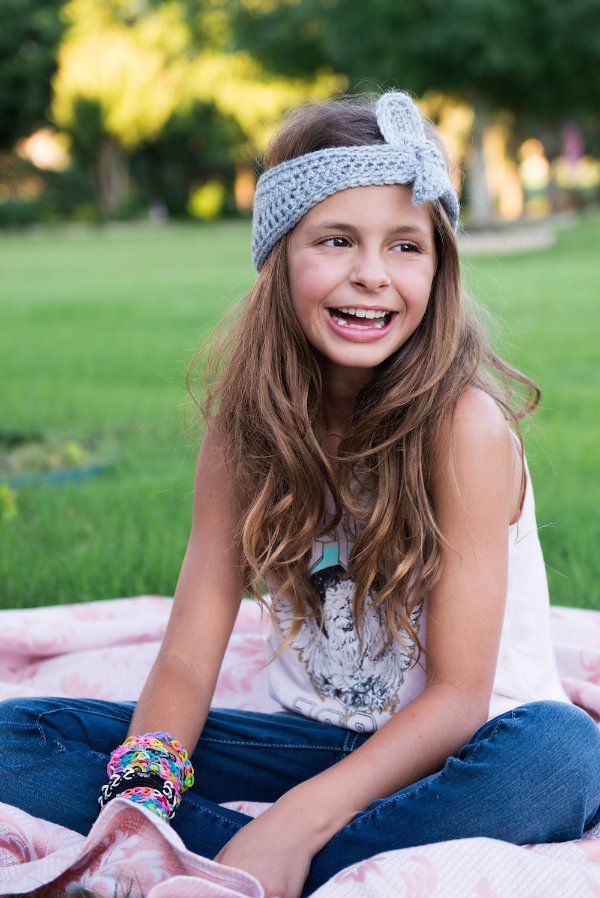 A girl sitting on a picnic rug wearing a knot=tie crochet headband.