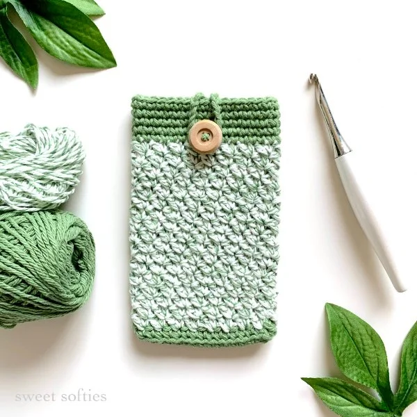 A green and white crochet e-reader case with yarn balls and a crochet hook.