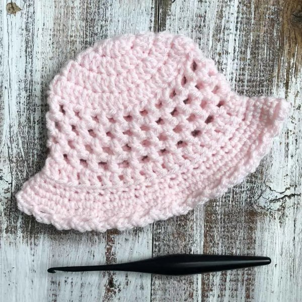 A pink child's sun hat and a crochet hook on a timber background.
