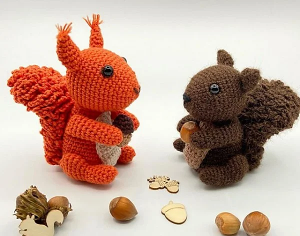 Two crochet squirrels with acorns facing each other on a white background.