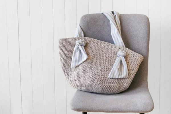 A crochet beach bag with fabric handles on a chair.
