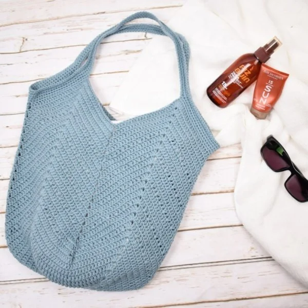 A blue, solid crochet beach bag with sunscreenand sunglasses.