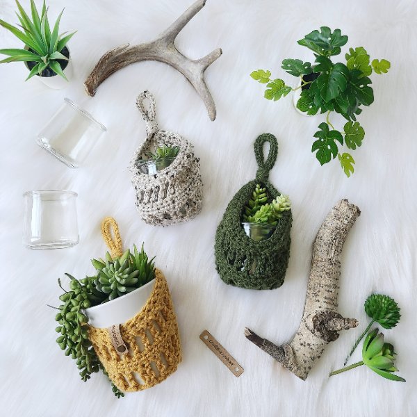 Three crochet hanging baskets holding plants on a white background.