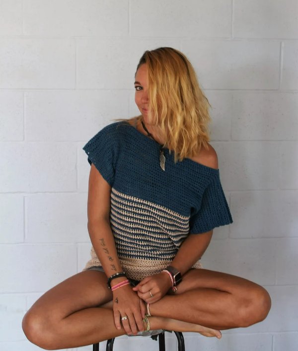 A woman sitting on a stool wearing a striped colour-blocked crochet tee.