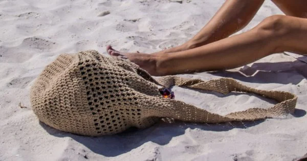 a crochet beachbag strewn on the sand.