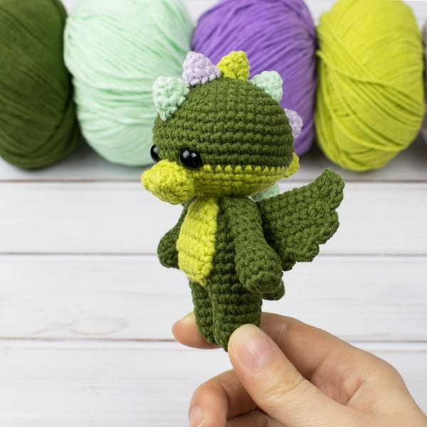 A small green crochet dragon with rainbow-coloured spikes.